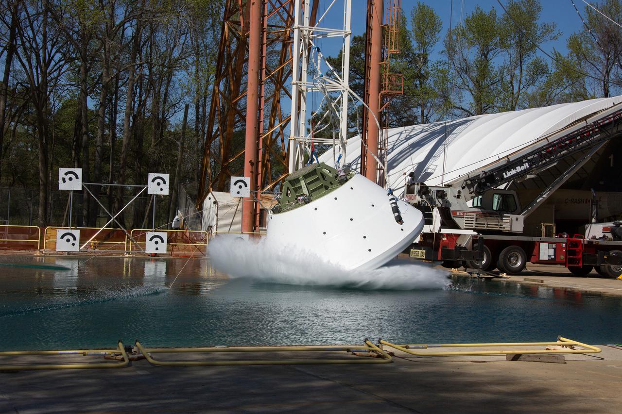 A white space capsule hitting the surface of a test pool at an angle, throwing up a sheet of spray