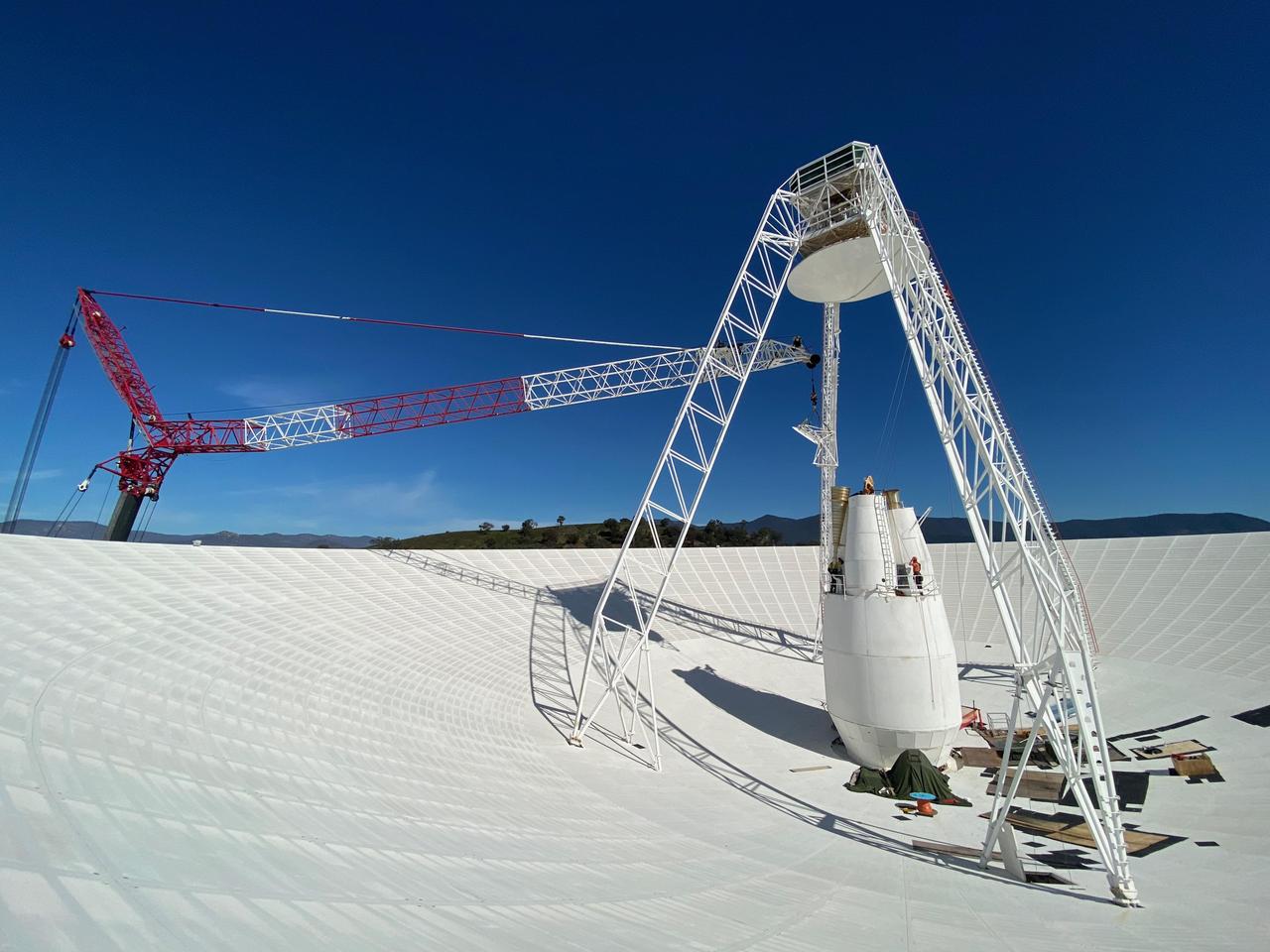 Workers and a crane dwarfed inside the white dish of a Deep Space Network antenna