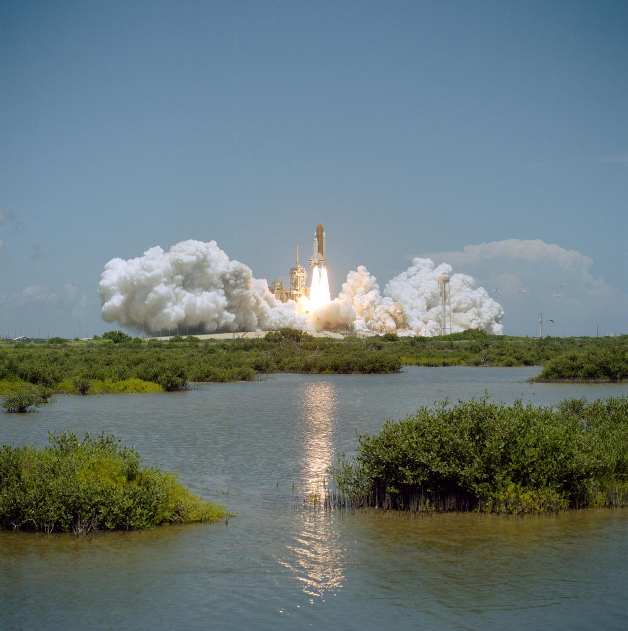 Space Shuttle Columbia lifting off across a marsh, exhaust reflected in the water